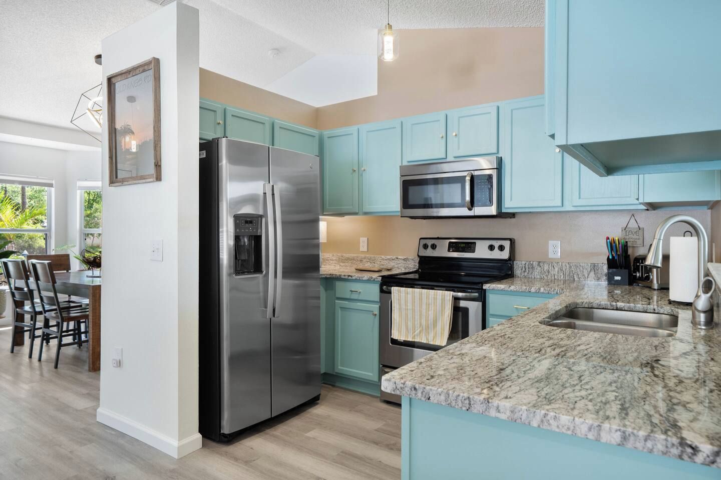 A modern kitchen with stainless steel appliances, teal cabinetry, and a granite countertop.