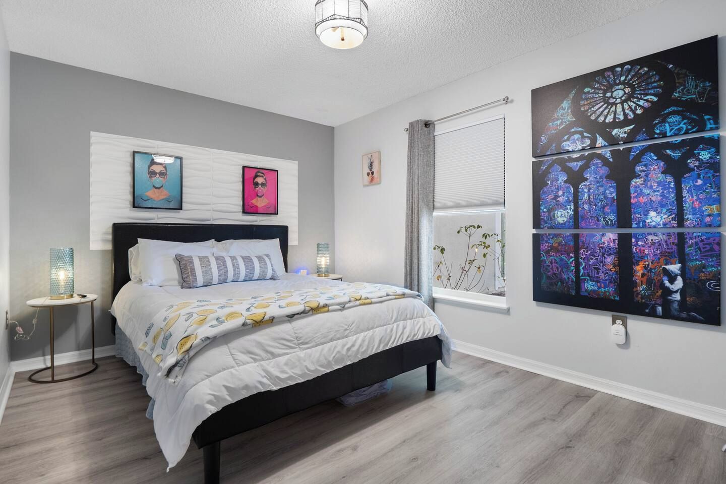 A bedroom with a bed, bedside lamps, a window with a view, and wall art.