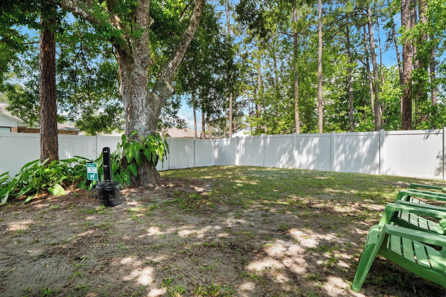 A backyard with a white fence, a tree, and a green bench.