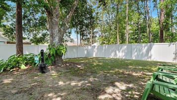 A backyard with a white fence, a tree, and a green bench.
