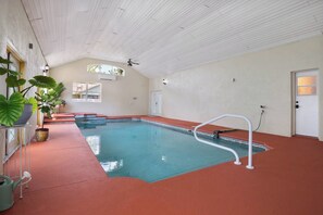 En indendørs swimmingpool med rødt gulv, hvidt loft og en dør til højre.