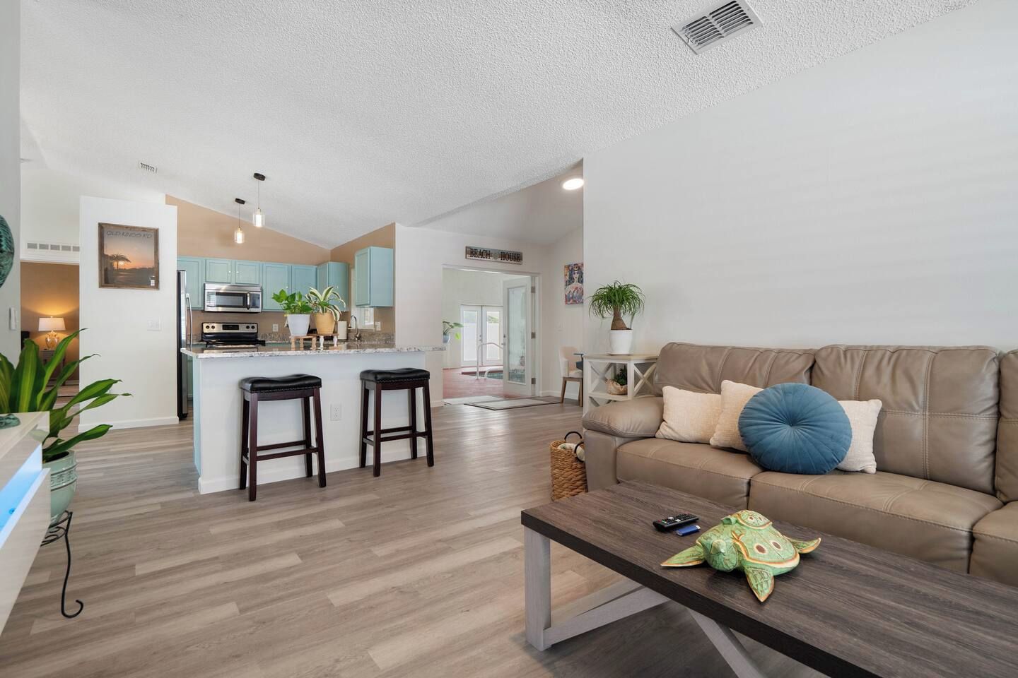 A modern living room with a brown leather sofa, a coffee table, and a kitchen area with light blue cabinets and a central island.