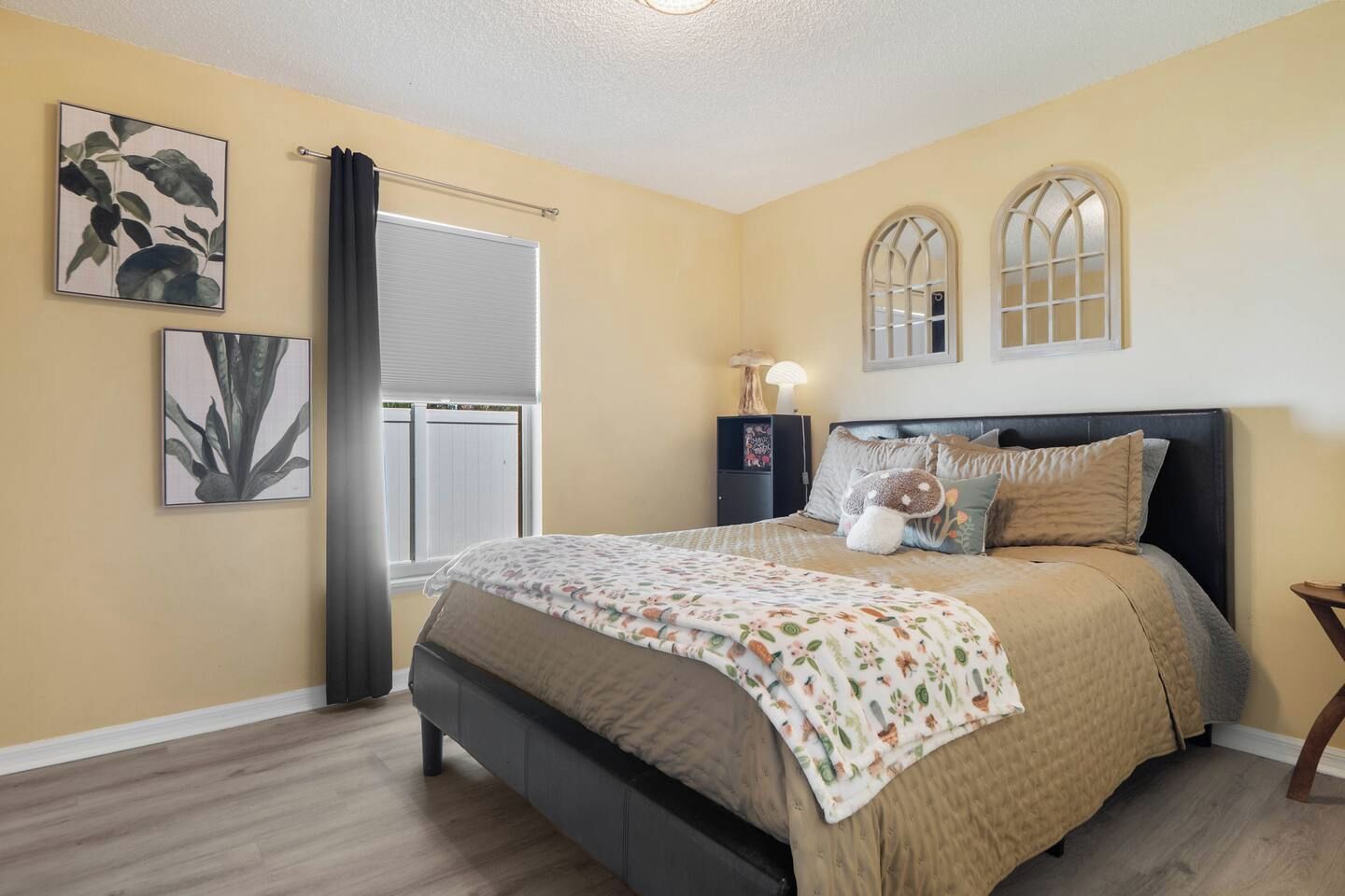 A bedroom with a bed, a window with curtains, a nightstand with a lamp, and two wall-mounted windows.