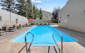 Piscina com guarda-sol vermelho, espreguiçadeiras e vista para árvores e colinas.