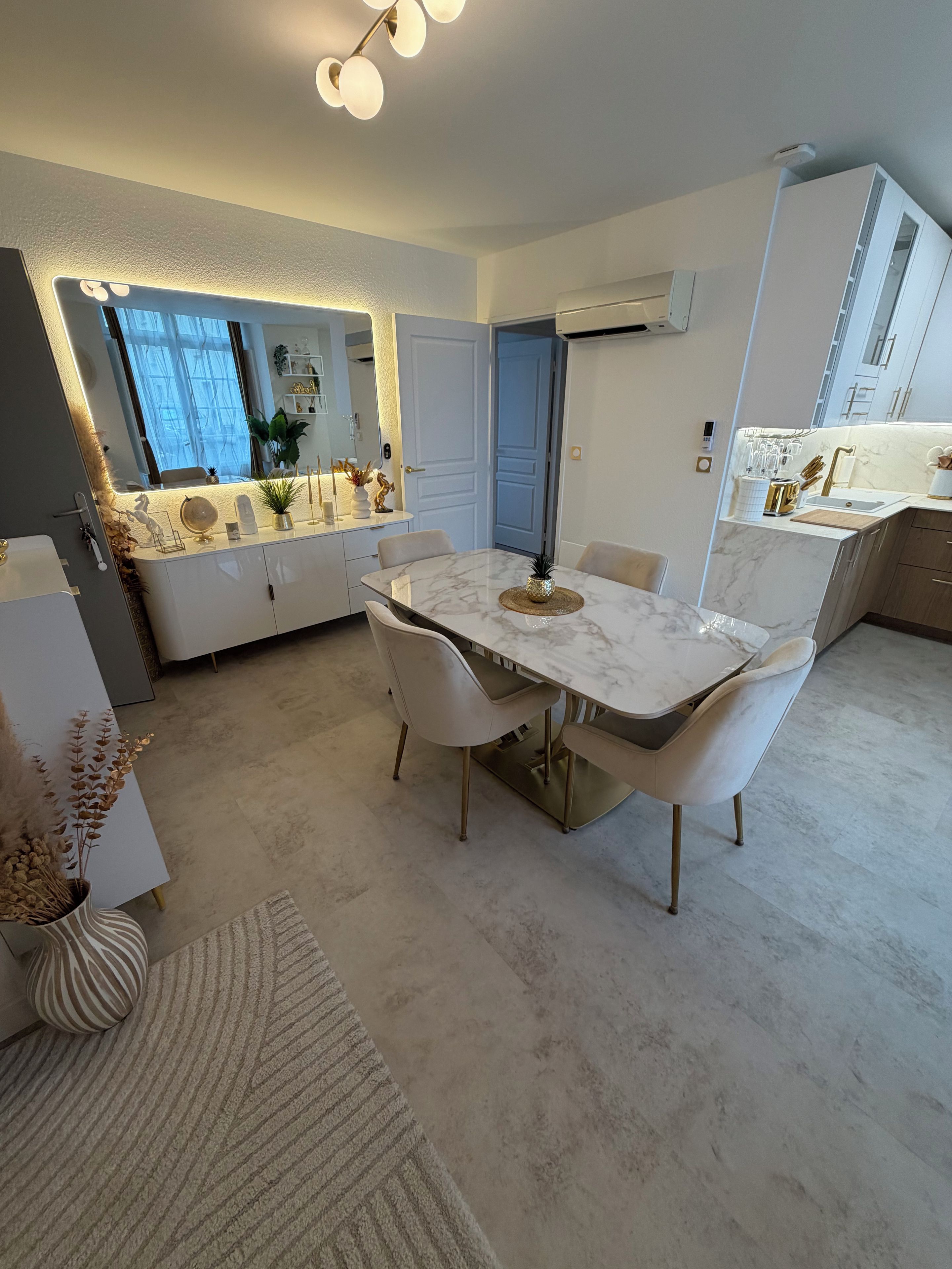 A modern kitchen with a marble countertop, white cabinets, and a dining area with a marble table and chairs.