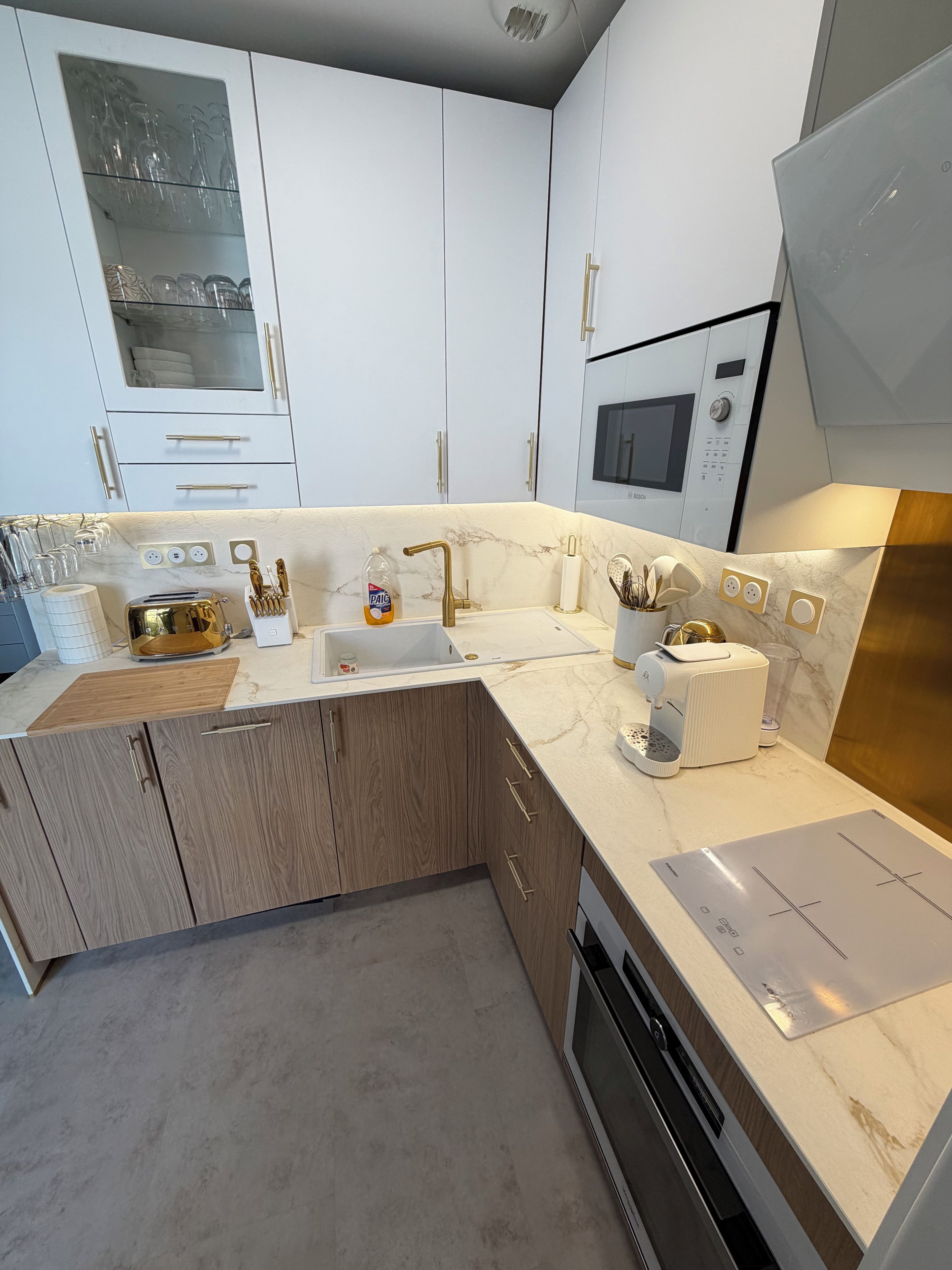 A modern kitchen with white cabinets, a marble countertop, a built-in oven, and a microwave.