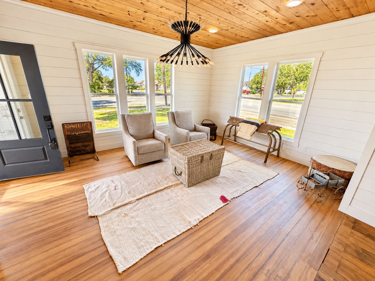 A spacious room with wooden floors, large windows, and a central seating area with chairs and a woven basket.