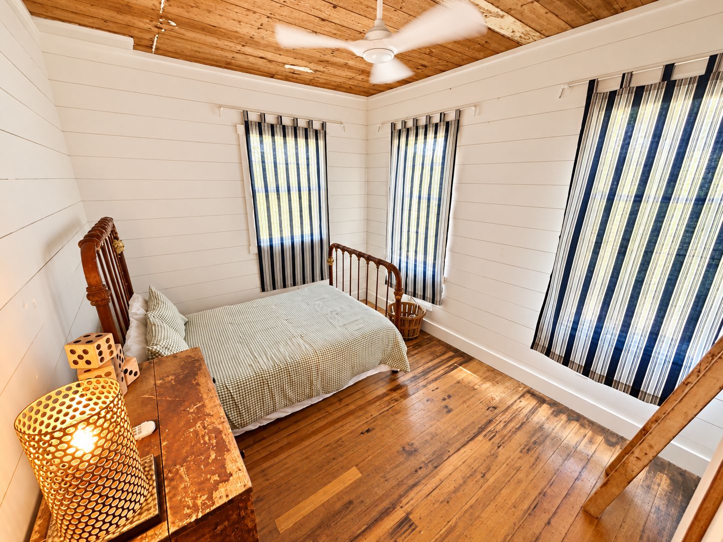 A bedroom with a wooden ceiling, a bed with a striped bedspread, a wooden chair, and a window with striped curtains.