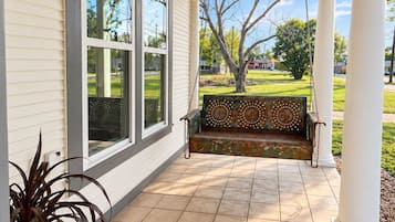 Eine überdachte Veranda mit einer Schaukel, einem Blumentopf und Blick auf eine grüne Landschaft.