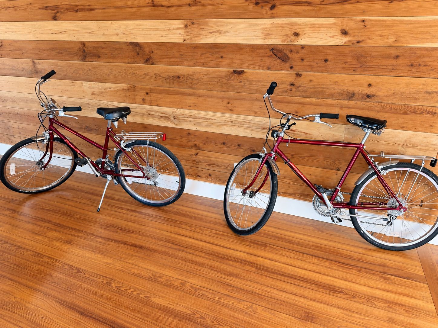 Two bicycles parked indoors against a wooden wall.