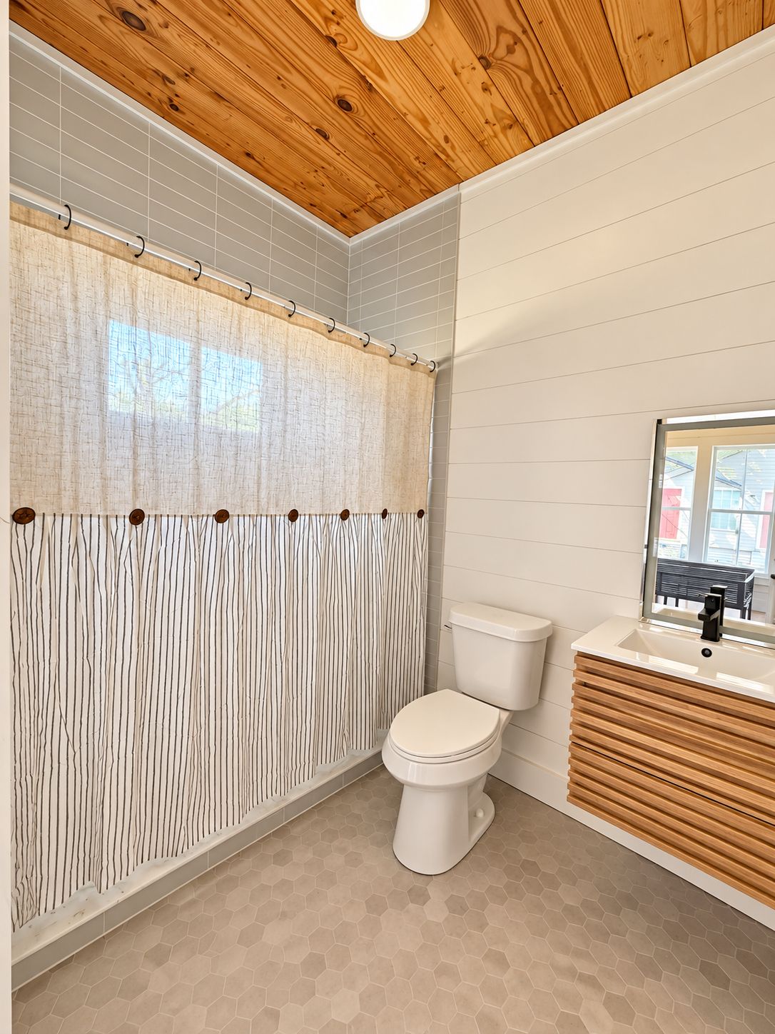Ein Badezimmer mit Holzboden, Duschvorhang, Toilette und Waschbecken mit Spiegel.