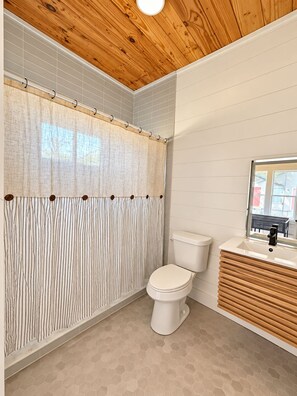 Un baño con techo de madera, cortina de ducha, inodoro y lavamanos con espejo.