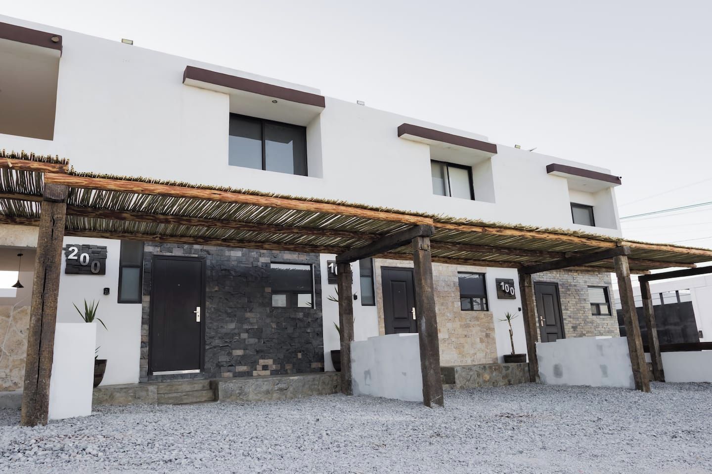 Un edificio moderno con acceso cubierto, unidades numeradas y suelo de grava.