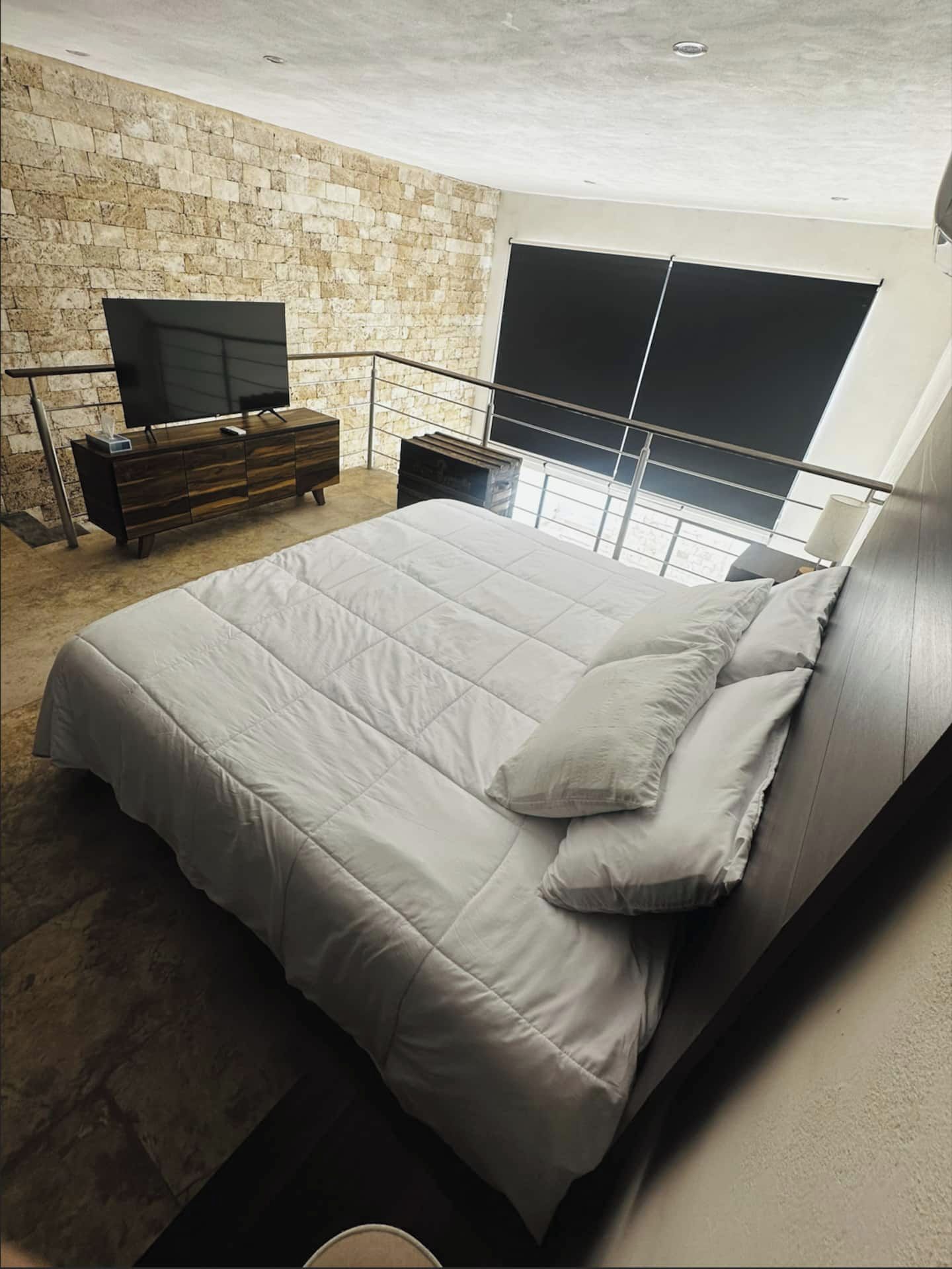 Un dormitorio moderno con una cama grande, un televisor y una pared de piedra.