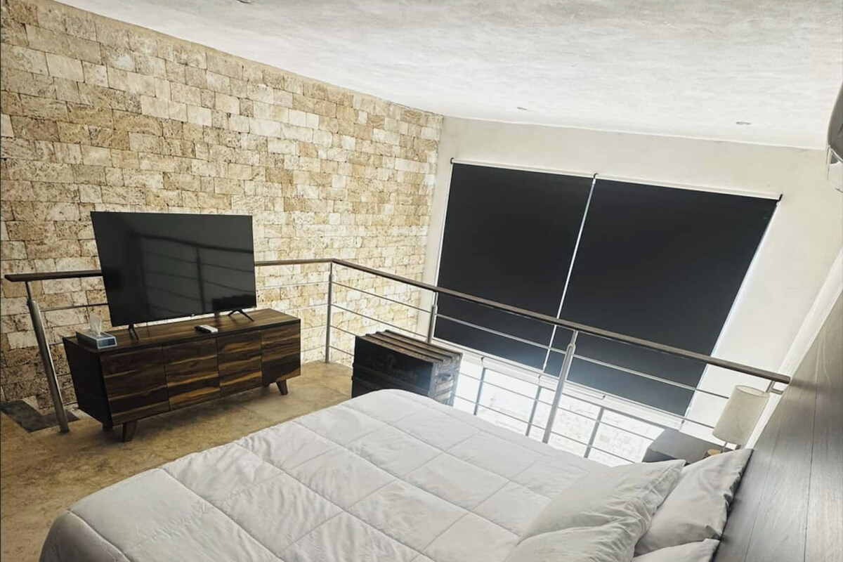 Une chambre moderne avec un grand lit, une télévision et un mur en pierre.