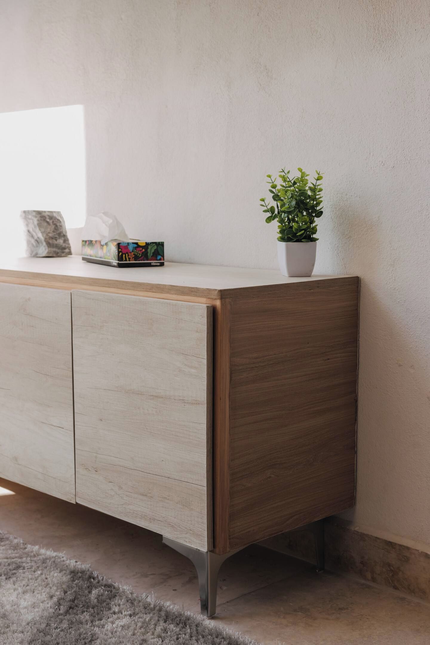 A wooden cabinet with a plant on top, a tissue box, and a framed picture.