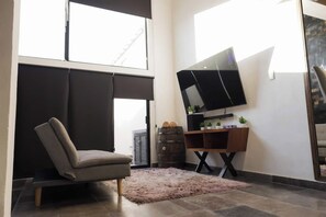 A modern living room with a sofa, a flat-screen TV mounted on a wooden stand, and a large window providing natural light. - Departamentos Madero (Parras de la Fuente)