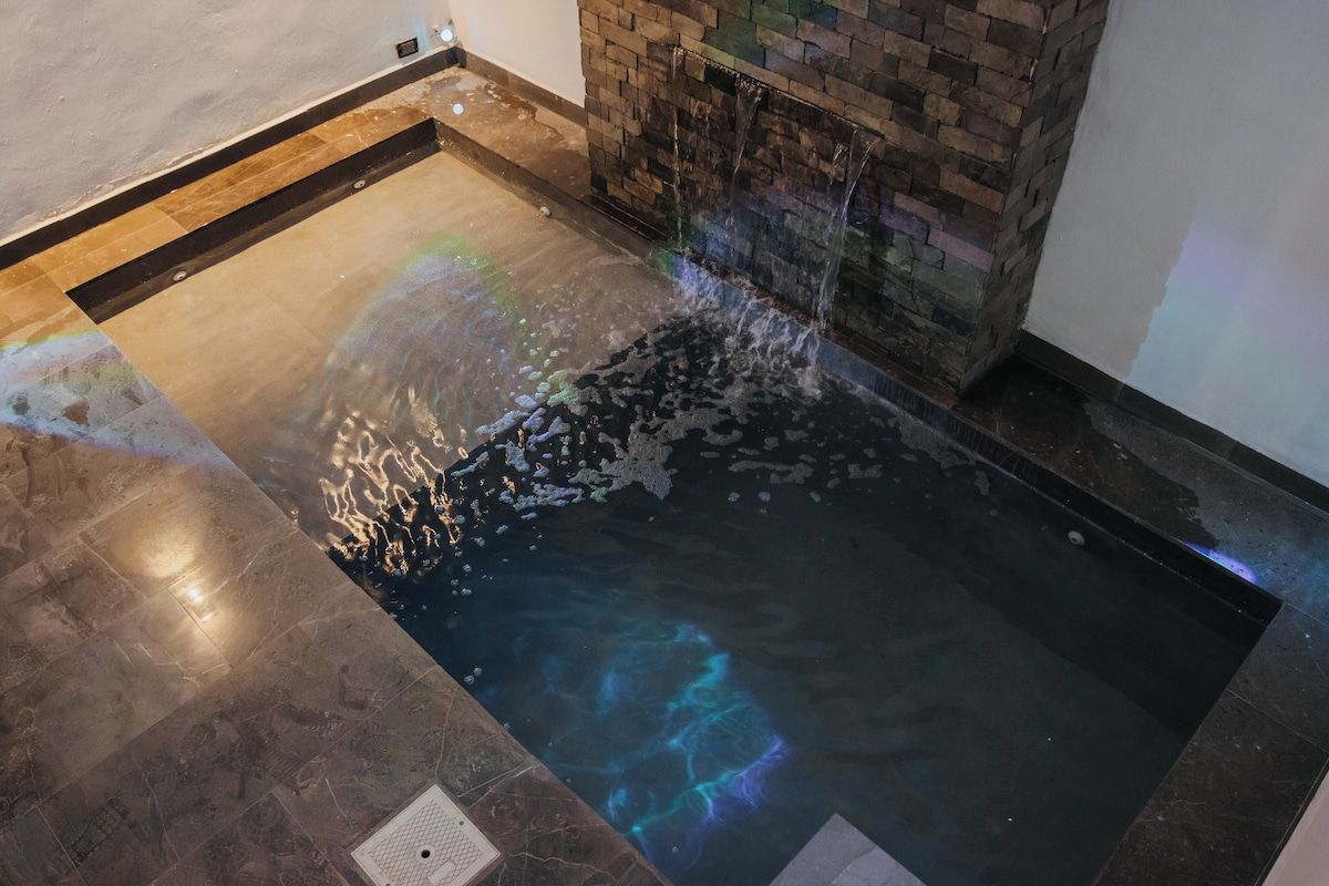 A spa area with a hot tub, a stone wall, and a tiled floor.