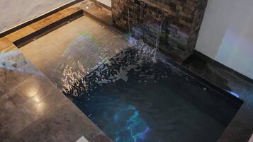 A spa area with a hot tub, a stone wall, and a tiled floor.