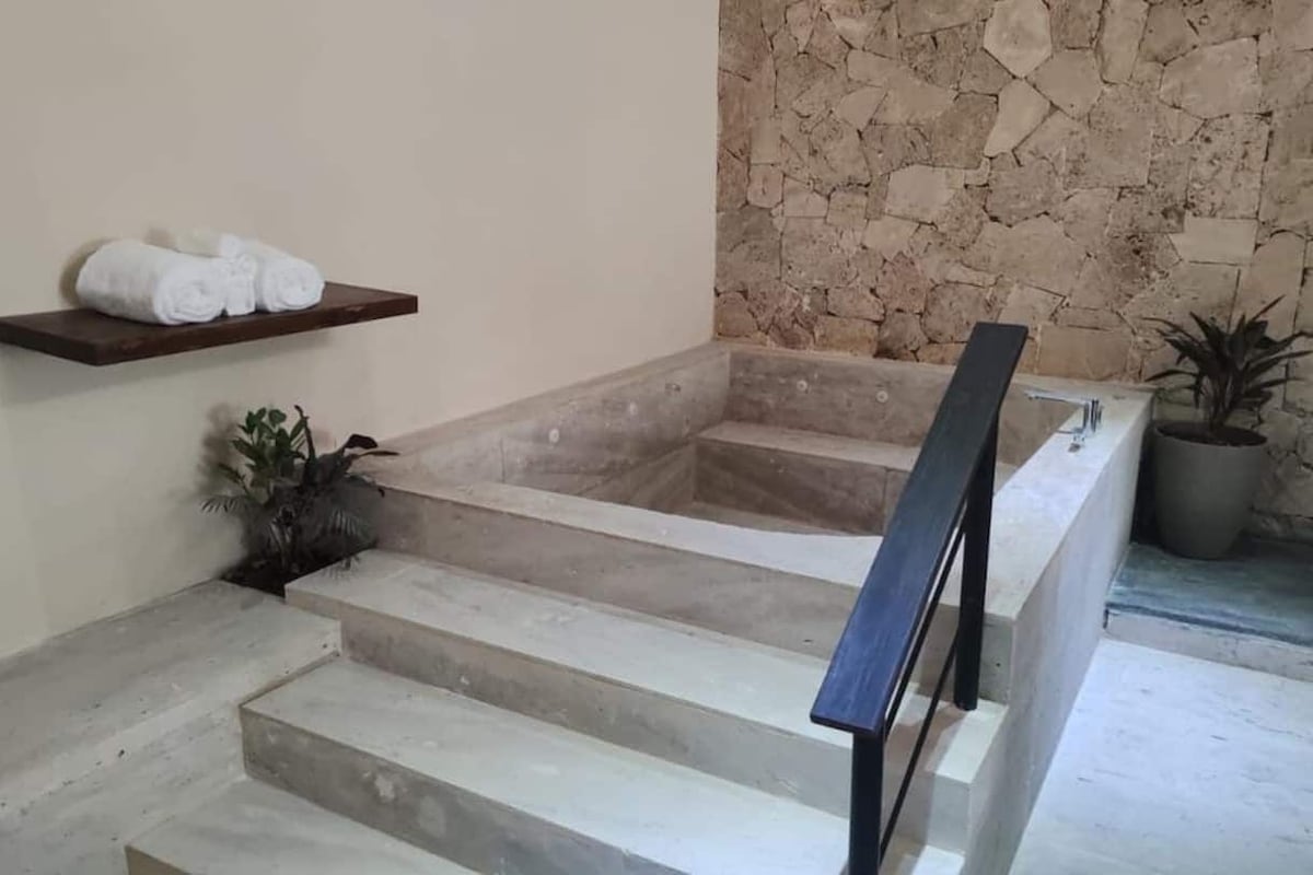 Zona de spa con pared de piedra, repisa de madera con toallas y una planta en maceta.