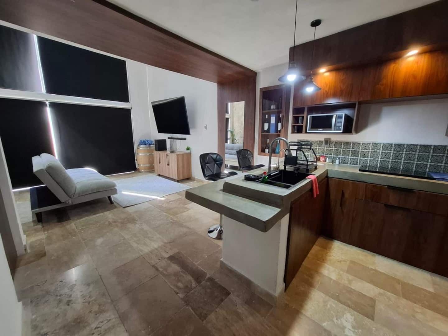Una cocina moderna con microondas integrado, un lavamanos y una zona de comedor con una silla.
