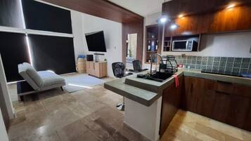 Una cocina moderna con microondas integrado, un lavamanos y una zona de comedor con una silla.