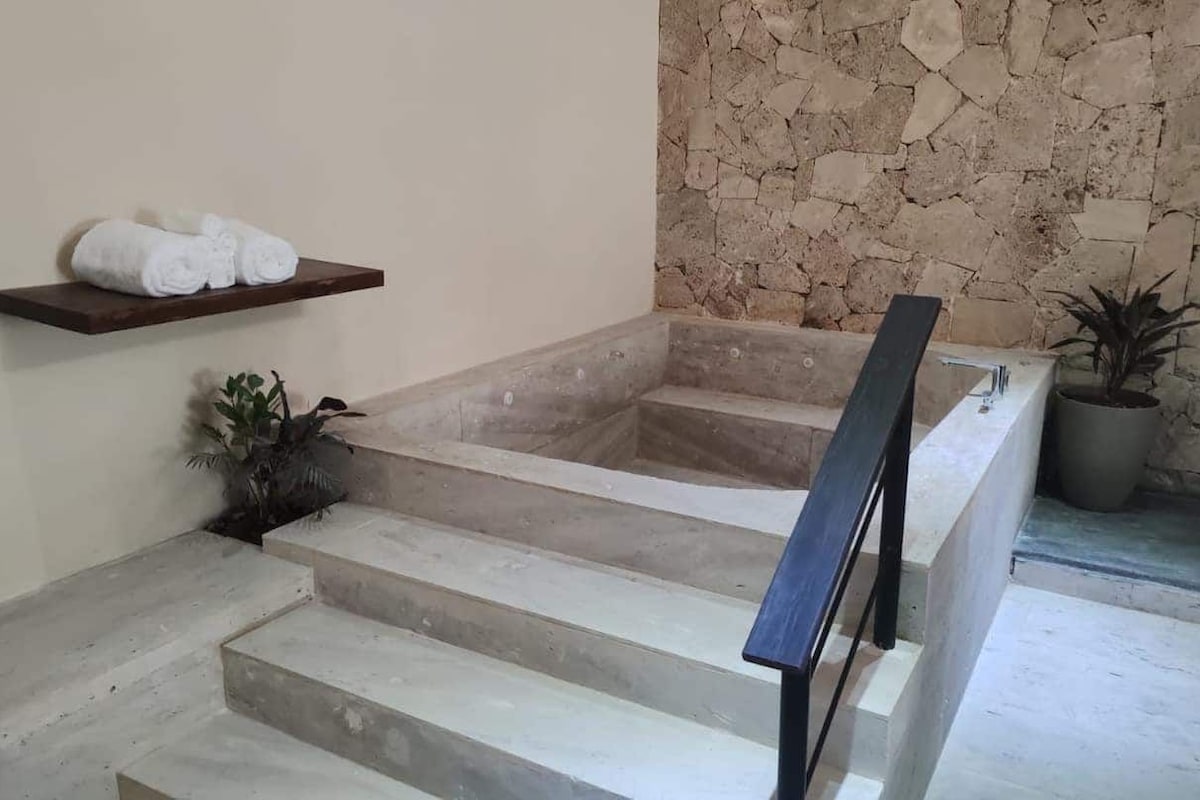 Un área de spa con pared de piedra, un estante de madera con toallas y una planta en maceta.
