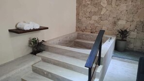 A spa area with a stone wall, a wooden shelf with towels, and a potted plant. - Departamentos Madero (Parras de la Fuente)