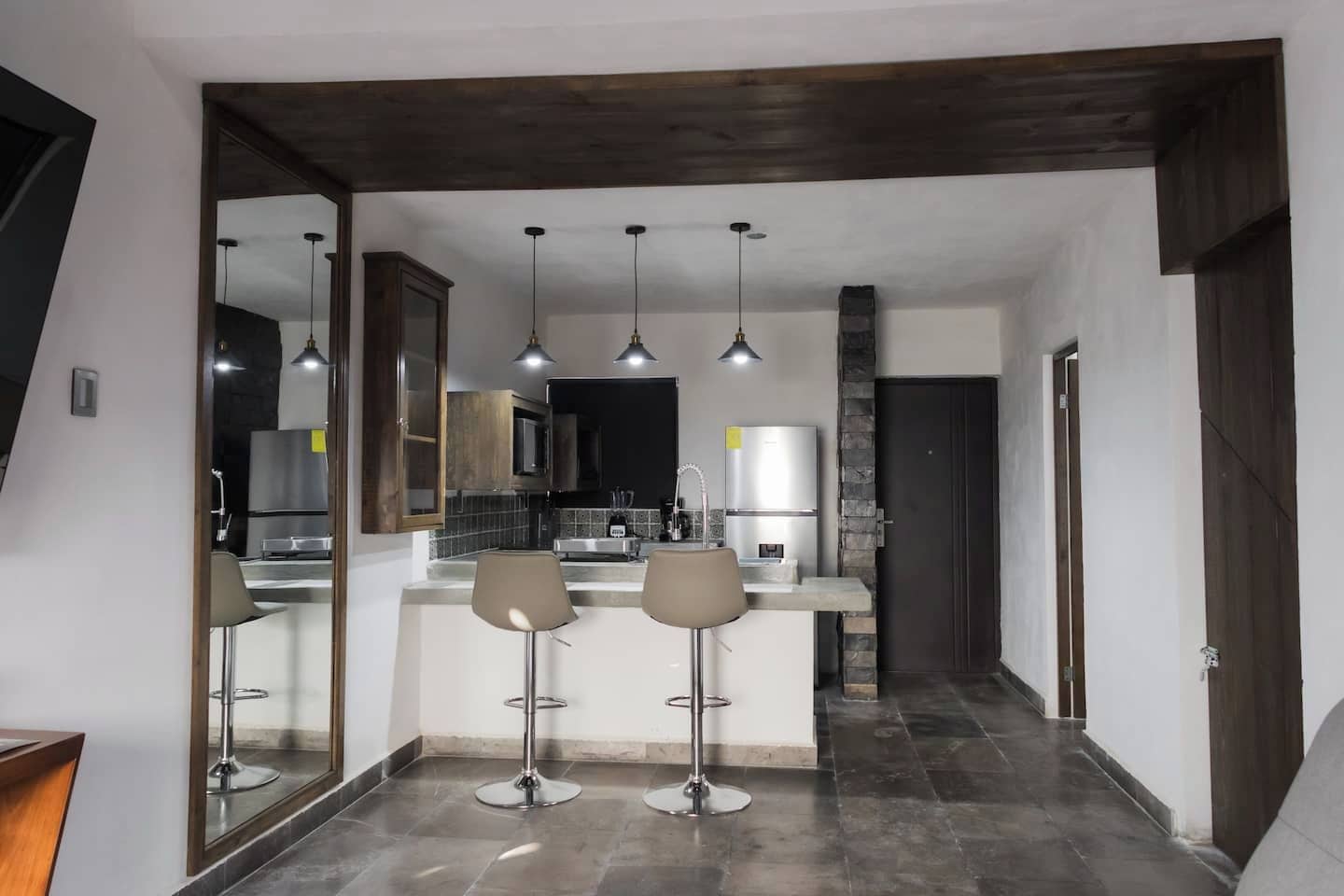 A modern kitchen with a central island, pendant lights, and a dark wooden ceiling.