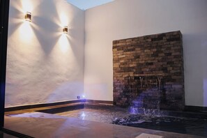 Un espace de détente avec un mur en pierre, un élément décoratif aquatique et des luminaires fixés au mur.