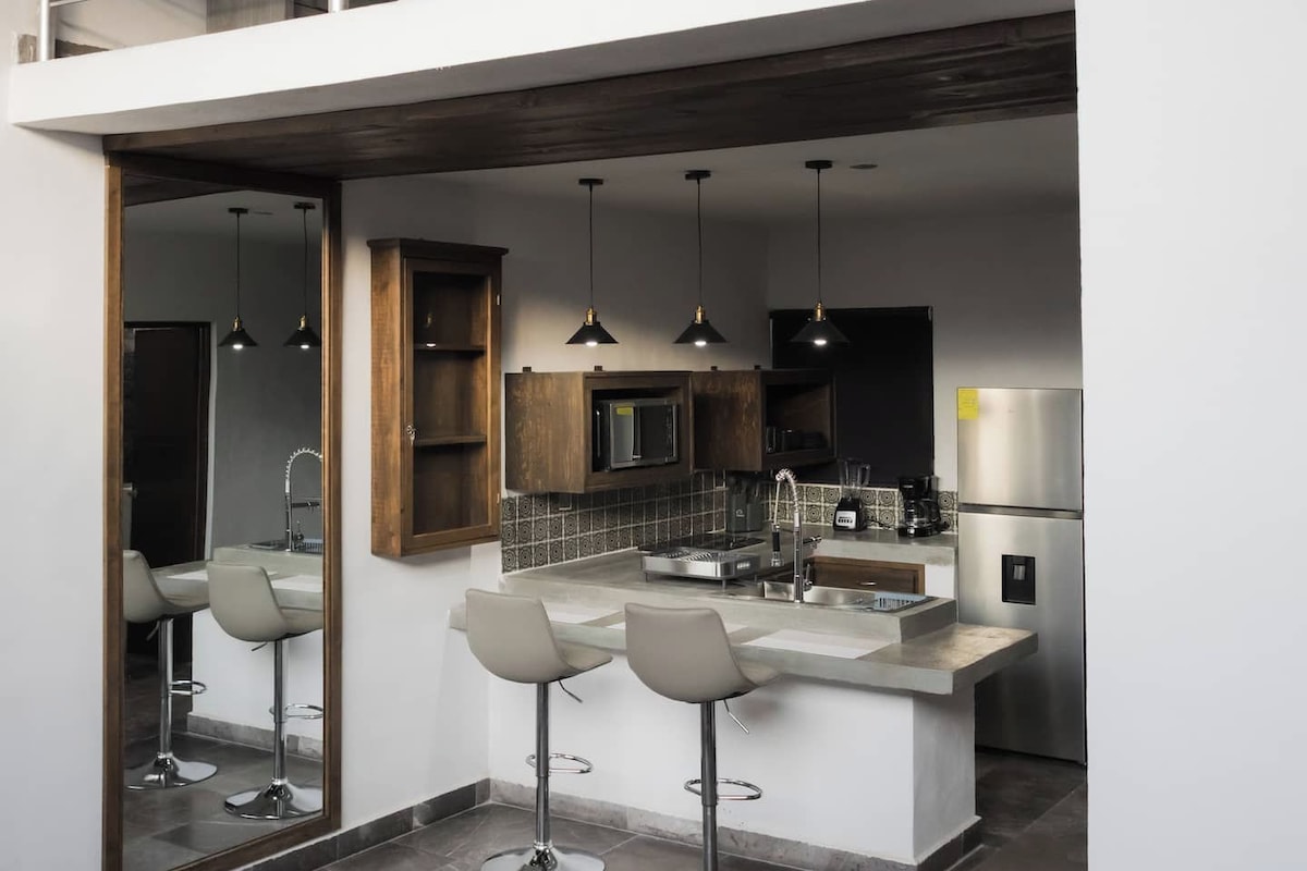Une cuisine moderne dotée d’un îlot central, de tabourets de bar et d’une mezzanine aménagée avec un lit.