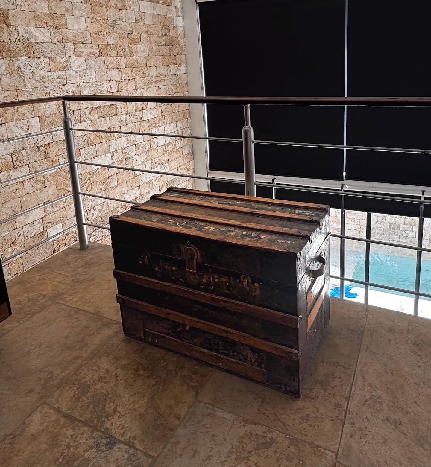 Un cofre de madera rústico y grande en una habitación con pared de piedra y barandilla de metal.