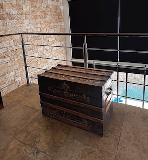 A large, rustic wooden chest in a room with a stone wall and a metal railing. - Departamentos Madero (Parras de la Fuente)