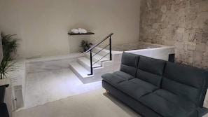 A modern interior with a staircase leading to a bathroom, a grey sofa, and a plant. - Departamentos Madero (Parras de la Fuente)