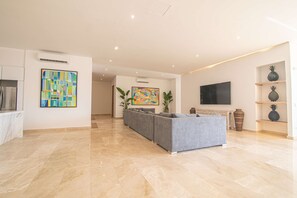 Amplia sala de estar con un sofá gris, un televisor de pantalla plana y dos cuadros abstractos en las paredes.