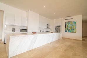 Una cocina moderna con armarios blancos, una isla de mármol y un cuadro abstracto y colorido en la pared.