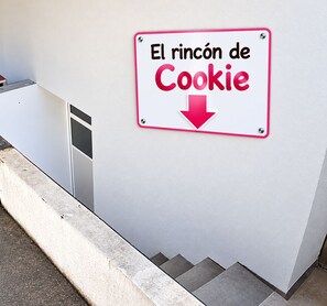 A sign with the text 'El rincón de Cookie' and a downward arrow, mounted on a wall next to a staircase. - New Listing (Bussigny)