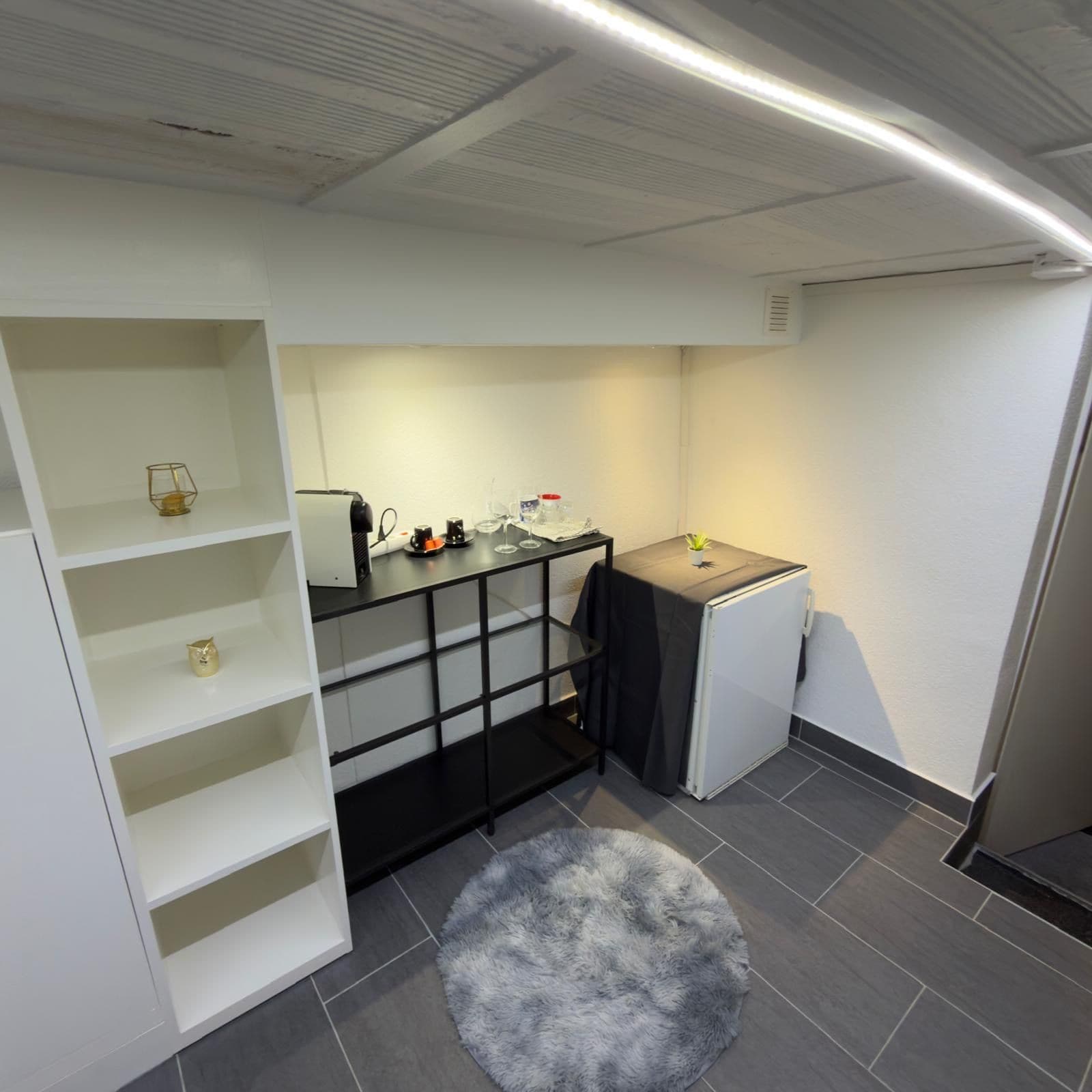 A compact kitchenette with a refrigerator, a coffee maker, and a small table.
