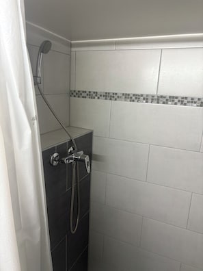 A shower with a handheld showerhead and a wall-mounted faucet, tiled walls, and a tiled shower floor. - New Listing (Bussigny)