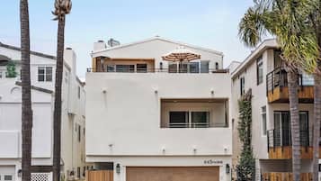 A modern two-story house with a garage, surrounded by palm trees and a clear sky.