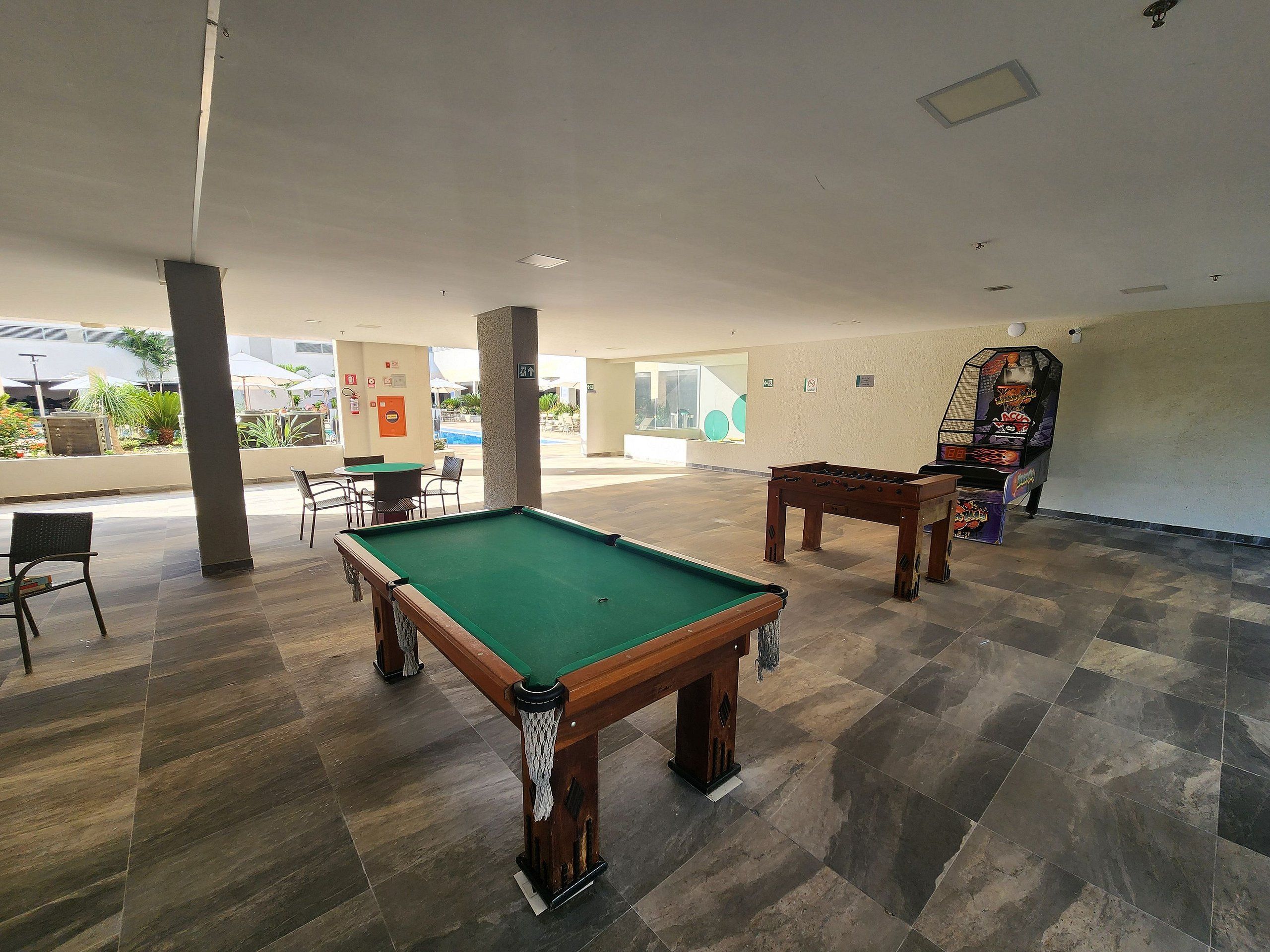 Espaço de lazer coberto com mesa de bilhar, mesa de futebol de mesa e área de estar com cadeiras e mesas.