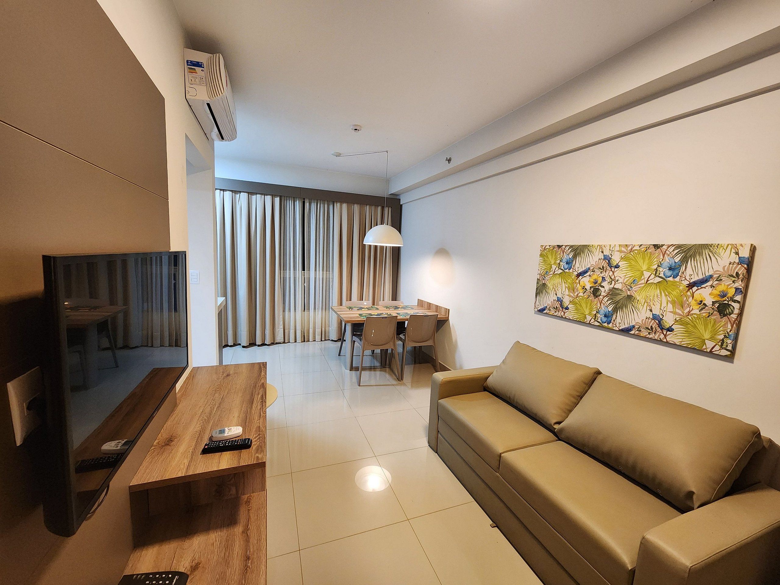 Uma sala de estar moderna com sofá, mesa de centro de madeira, área de jantar com mesa e cadeiras, e uma janela grande com cortinas.