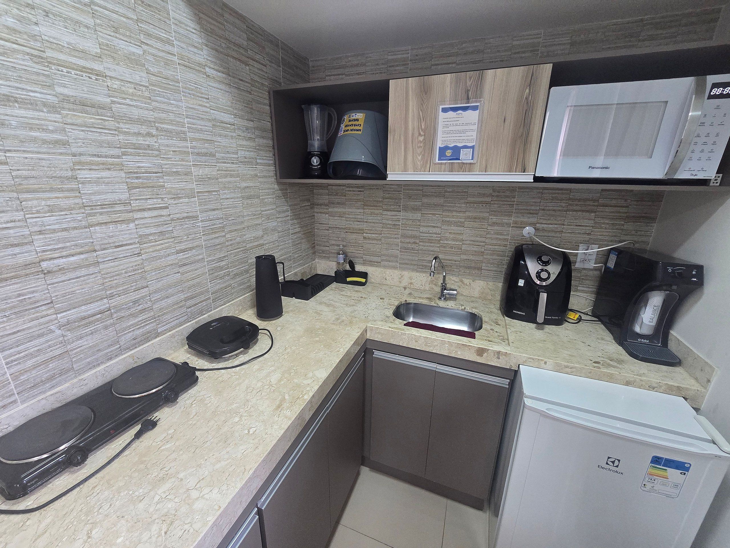 Una cocina equipada con microondas, cafetera y un refrigerador pequeño.