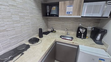 Una cocina equipada con microondas, cafetera y un refrigerador pequeño.