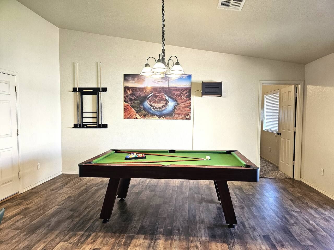 Ein Billardtisch in einem Raum mit Holzboden, einem Gemälde an der Wand und einer Tür im Hintergrund.