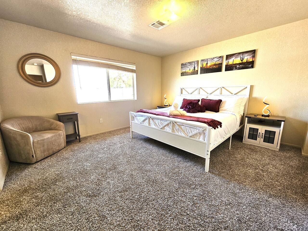 A bedroom with a bed, a chair, a nightstand, a window, and wall art.
