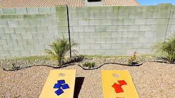 Dos tablas de madera con formas recortadas sobre un lecho de grava, un muro de ladrillo y un cielo azul despejado.