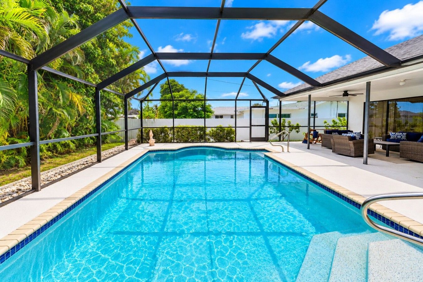 A swimming pool with a glass enclosure, surrounded by outdoor furniture and a view of the sky.
