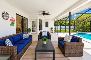 Un patio couvert aménagé avec des meubles en osier, un ventilateur de plafond et une vue sur une piscine.