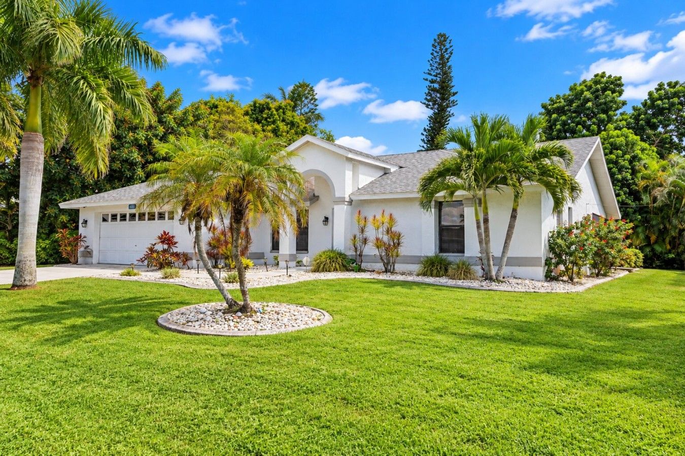A modern two-story house with a white exterior, a garage, and a well-maintained lawn with palm trees.